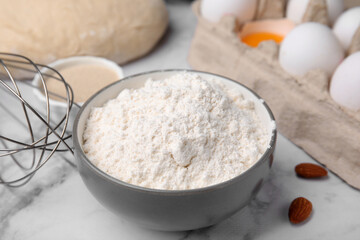 Fototapeta na wymiar Bowl with flour on white marble table, closeup