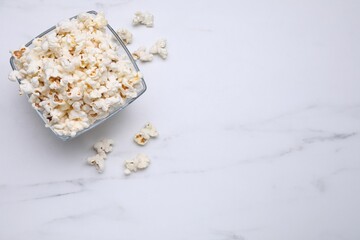 Bowl of tasty popcorn on white marble table, flat lay. Space for text