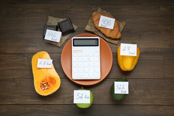 Calculator and food products with calorific value tags on wooden table, flat lay. Weight loss concept
