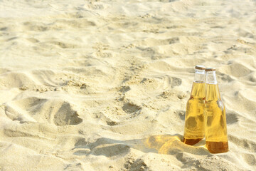 Bottles of cold beer on sandy beach near sea, space for text