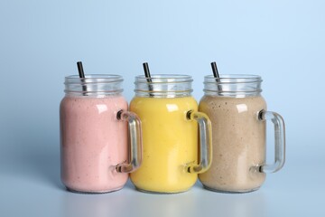 Mason jars with different smoothies on light blue background