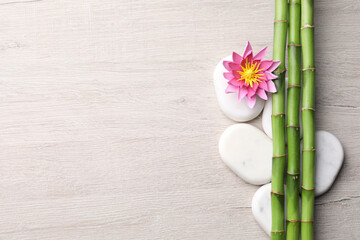 Spa stones, flower and bamboo stems on light wooden table, flat lay. Space for text