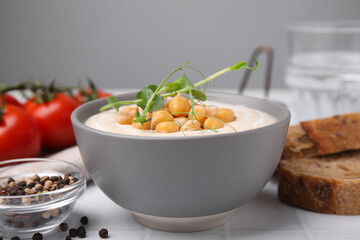 Tasty chickpea soup in bowl on white tiled table, closeup