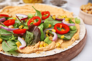 Tortilla with hummus and vegetables on table, closeup