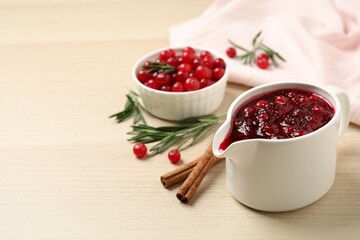 Cranberry sauce in pitcher on wooden table, space for text