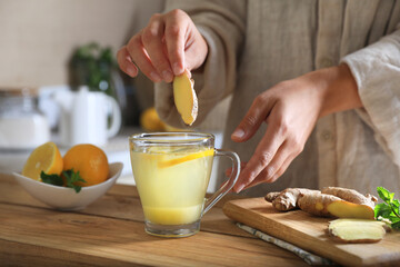 Woman making aromatic ginger tea at wooden table indoors, closeup