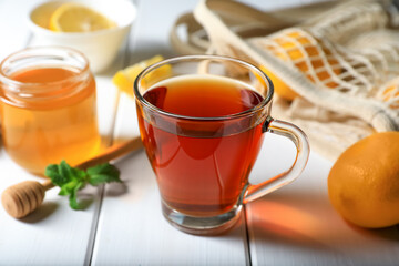 Cup of delicious ginger tea and ingredients on white wooden table, closeup