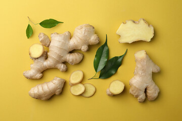 Fototapeta premium Fresh ginger with green leaves on pale light yellow background, flat lay
