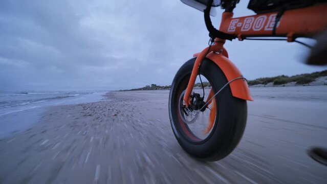 Man cycling on a beach close wheel shot orange electric bike France Occitanie
