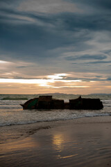 An old and rusty shipwrecked on the beach with the sunset in the background