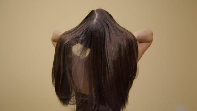Luxurious long brunette hair in slow motion. Back view. Yellow background.