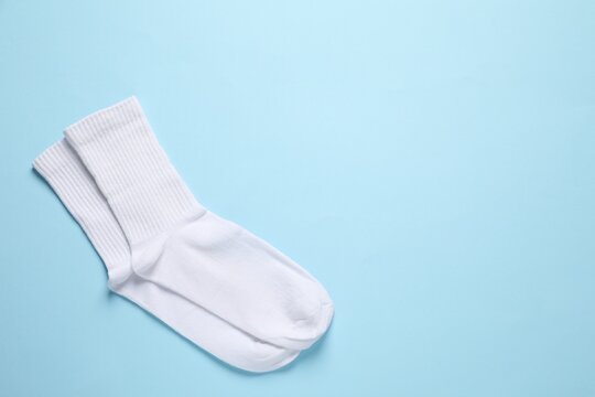 Pair of white socks on light blue background, flat lay. Space for text