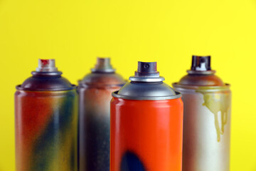 Used cans of spray paints on yellow background, closeup