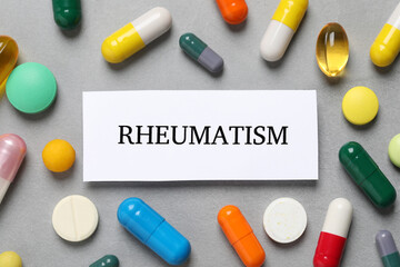 Sheet of paper with word Rheumatism and many different pills on light grey table, flat lay