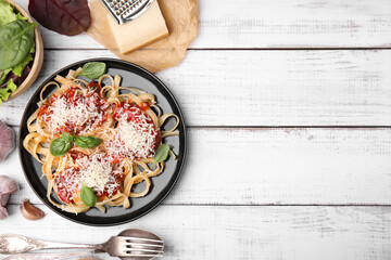 Delicious pasta with tomato sauce, basil and parmesan cheese on white wooden table, flat lay. Space for text