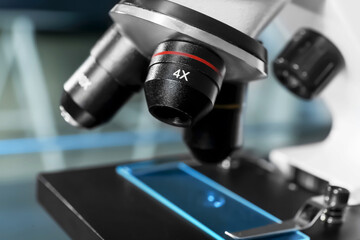 Modern medical microscope with glass slide on blurred background, closeup