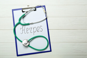 Clipboard with word Herpes and stethoscope on white wooden table, top view. Space for text