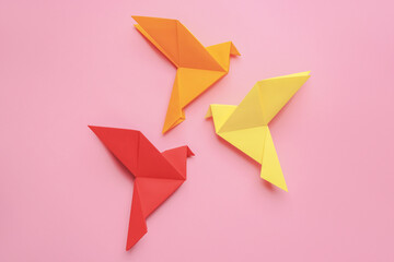 Beautiful colorful origami birds on pink background, flat lay