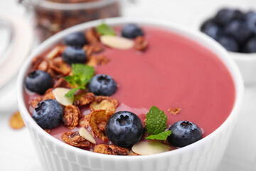 Bowl of delicious smoothie with fresh blueberries and granola on white table, closeup