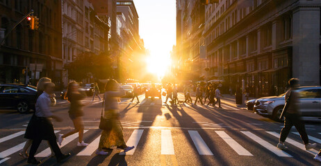 Crowds of diverse people and cars traveling through a busy intersection on 5th Avenue and 23rd Street in New York City with sunlight in the background