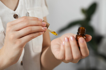 Young woman applying essential oil onto wrist on blurred background, closeup