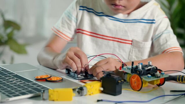 Asian kid boy plugging energy and signal cable to sensor chip with Arduino robot car, Little child remotely learn online with car toy, STEAM education AI technology course school learning lesson