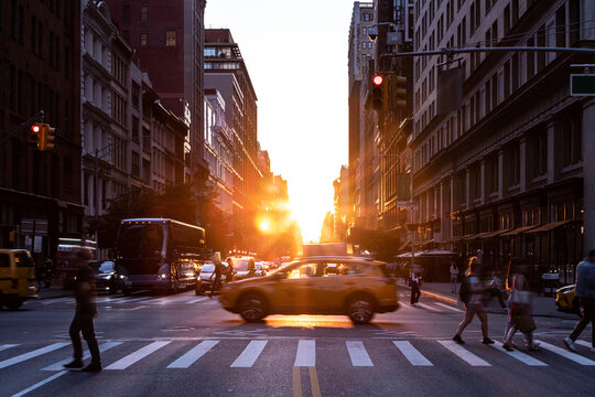 Taxi driving through a busy intersection past the people in the intersection of 5th Avenue and 23rd Street in New York City with sunset background