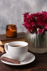 Beautiful pink chrysanthemum flowers and cup of aromatic tea with sweet chocolate cookie on wooden table