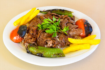 Turkish and Arabic Traditional Ramadan doner kebab with tasty tomato sauce and rice or turkish pilav in white plate on wood table background. ( Pilav ustu doner)