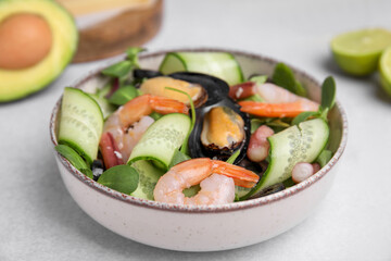 Bowl of delicious salad with seafood on light grey table, closeup