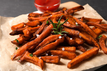 Delicious sweet potato fries and sauce on parchment paper, closeup