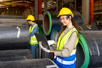 Asian engineer worker inspecting inside the metal sheet steel manufacturing factory while looking at the laptop for monitoring the improvement of capacity and productivity