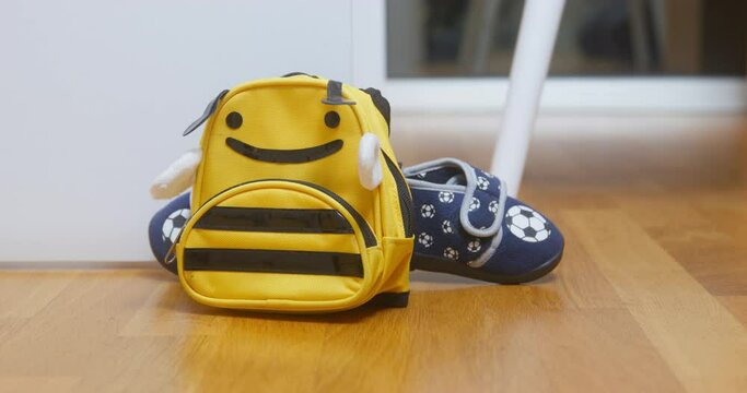 Someone throws a yellow backpack in the shape of a bee with small sneakers on the floor, close up, low-angle front view. Child returned home from training.