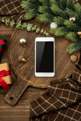 Smart phone on wooden cutting board with Christmas decorations.