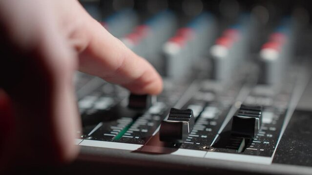 Man's finger increase the volume on the sound control panel mixer - close-up