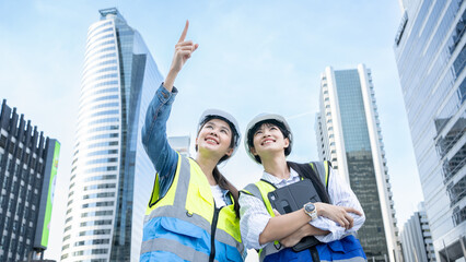 Portrait of two professional Asian engineer or technician workers stand look at camera with smiling and arm-crossed on City  of construction site and day light. Woman in Engineering project manager.