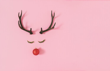 Naklejka premium Trendy Christmas composition made of evergreen for, red bauble decoration and antlers on pastel pink background. Creative art minimal aesthetics..Minimal winter holidays idea. Flat lay, top view