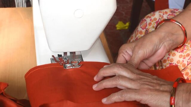 Close up view of female hands stitching fabric on sewing machine at workplace or home. Hands holding textile for dress production. Concept of self employment woman and Female entrepreneurs in India.