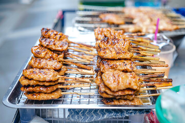 Milk marinated pork skewered on bamboo grills over charcoal for sale along the sidewalk in Bangkok, Thailand.