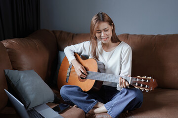Portrait of young asian woman playing guitar on sofa relaxing stress on vacation