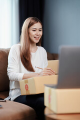 Starting small business entrepreneur of independent young Asian woman online seller is using computer and taking orders to pack products for delivery to customers. SME delivery concept