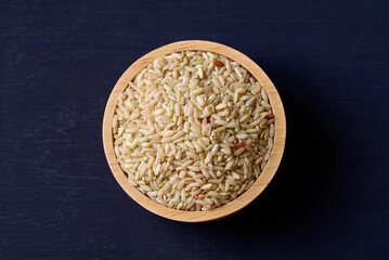 Fototapeta na wymiar Organic Thai brown rice grain in wooden bowl on black background, Asian healthy food ingredients