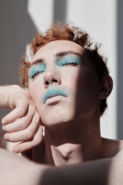 Close up low angle portrait of young man with eyes closed wearing modern blue make-up