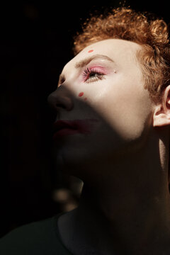 Close up portrait of young queer man with curly red hair looking away in contrast light