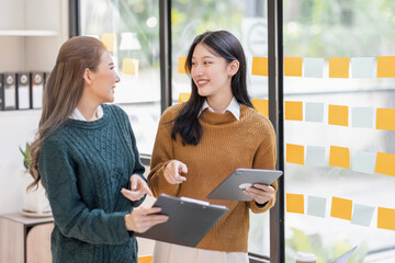 Two Asian women analyzing documents while sitting on a table in office. Woman executives at work in office discussing some paperwork.