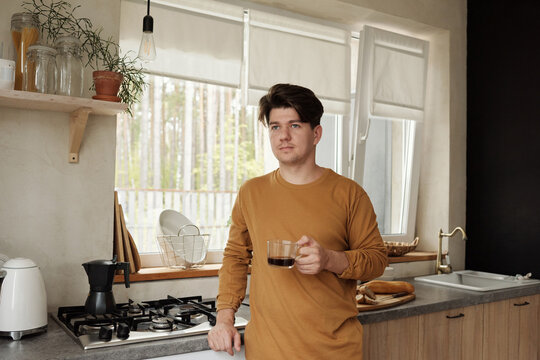 Caucasian man wearing casual outfit holding cup of coffee standing looking away in kitchen horizontal medium shot