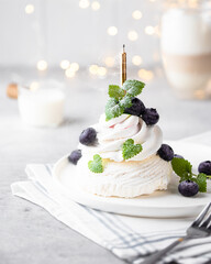 Meringue cake with cream on a white background in a modern interior. The cake is decorated with mint and blueberries