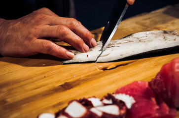 Close up of Chef cook hands chopping Saba fish for traditional Asian cuisine with Japanese knife. Professional Sushi chef cutting seafood japanese chefs are making Saba fish sashimi. Dark Tone