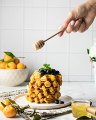 A woman pours honey on Viennese waffles with tangerines. Waffles are decorated with mint.