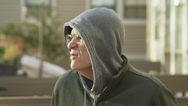 Tight crop clip of an old man in his late 50's zips up his hood and reacts to colder weather